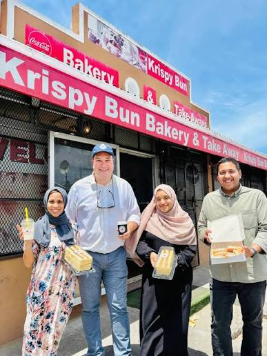 Customers and the local Mayor outside Krispy Bun Bakery, holding fresh takeaway cakes